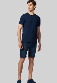 Granatowa bawełniana koszulka z okrągłym dekoltem, zestawiona z szortami dżinsowymi z podwiniętymi rękawami, dopełniona granatowymi trampkami.