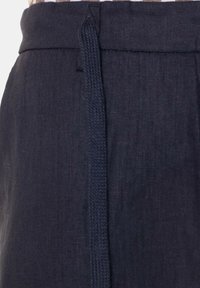 Pantaloni di lino blu scuro con vita piatta e dettaglio in tessuto intrecciato per la chiusura. Il tessuto ha una consistenza liscia e una leggera lucentezza.