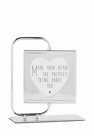 Silberner Metallrahmen mit herzförmigem Ausschnitt, der den Text "Make your heart the prettiest thing about you" auf weißem Hintergrund anzeigt.