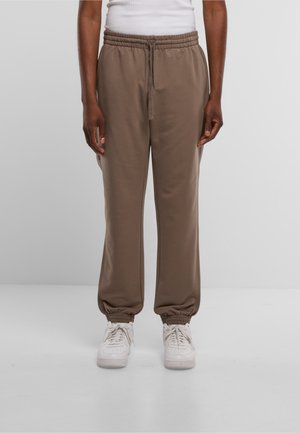 Brown, elastic waistband joggers with gathered cuffs, designed for comfort, paired with white sneakers on a plain background.