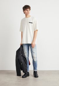 Kremfarget bomullst-skjorte med lomme foran; lyseblå slitte jeans; svart skinnjakke lagt over armen; svarte ankelboots.