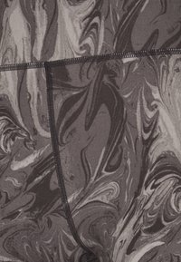 Tessuto marmorizzato in nero e grigio con una texture che ricorda delle spirali. Presenta una cucitura nera a contrasto lungo il bordo.