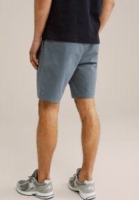 Modri bombažni kratki hlače z stranskimi žepi, sproščenega kroja in obrnjeno robom, v kombinaciji z sivimi tekaškimi čevlji. Brez posebnih vzorcev.