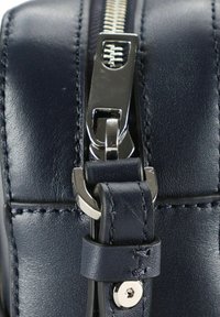 Borsa in pelle blu navy con zip e accessori in metallo argentati. La vista ravvicinata evidenzia i dettagli delle cuciture e della tracolla con accenti in metallo.