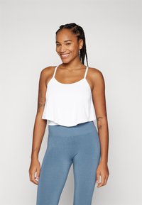 Weißes, kurzes Tanktop mit dünnen Trägern, kombiniert mit hochtaillierten blauen Leggings. Glatte Textur, einfaches Design, geeignet für Sportbekleidung.
