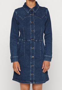 Granatowa sukienka z denimu z długimi rękawami, zapinana na guziki z przodu, dopasowana w talii, z klasycznym kołnierzem, noszona przez osobę na jednolitym tle.