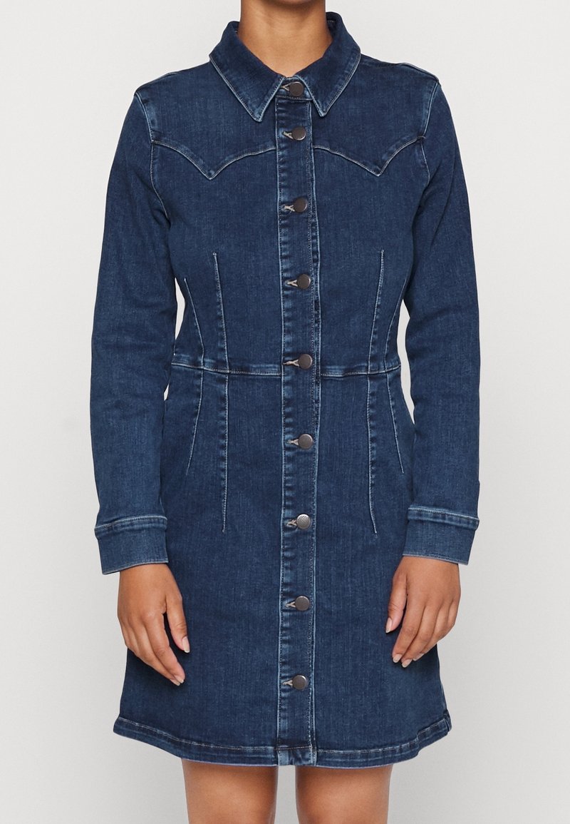 Granatowa sukienka z denimu z długimi rękawami, zapinana na guziki z przodu, dopasowana w talii, z klasycznym kołnierzem, noszona przez osobę na jednolitym tle.