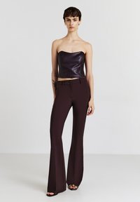 Top nero senza spalline in pelle abbinato a pantaloni bordeaux aderenti a zampa. Il top presenta un design strutturato, mentre i pantaloni hanno una texture liscia.