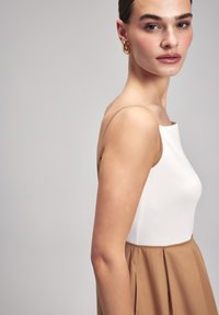 Liivitu dresses sombanais saket mai pavan videl inge majvi white bodice ja flowing beige skirt. Pehmea kangas, millel on sujuv tekstuur ja õrnad pleatide detailid.