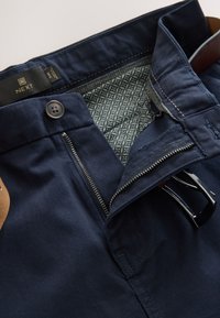 Navy blue trousers with button and zipper open, showing patterned inner fabric and a black belt with a silver buckle.