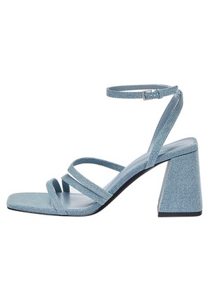 Blue denim heeled sandals with a square toe, featuring multiple crossed straps and a wide block heel. Smooth texture with a light tone.