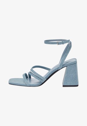 Sandalias de tacón de mezclilla azul con punta cuadrada, con múltiples tiras cruzadas y un tacón ancho de bloque. Textura suave con un tono claro.