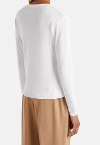 Biały sweter z długim rękawem, z okrągłym dekoltem, z prążkowanym wykończeniem na dole i mankietach, gładką fakturą i standardowym krojem, zestawiony z beżowymi spodniami.