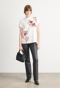 Witte short-sleeve top met roze bloemenprint, gecombineerd met zwarte leren broeken en een kleine geweven zwarte handtas. Zwarte hoge hakken.