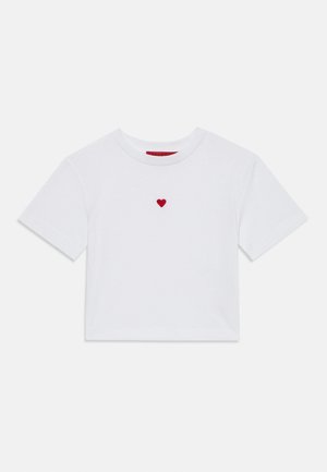 T-shirt court blanc en coton avec un petit cœur rouge brodé sur la poitrine. Encolure ronde simple et manches courtes.
