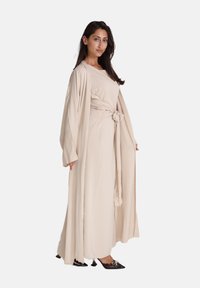 Beige lange jurk met een geknoopte taille, gelaagd met een losse, open voorkant buitenkleding, gemaakt van een gladde stof met een zachte textuur.