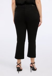 Černé denimové kalhoty s rozšířenými nohavicemi, středně vysokým pasem, pěti kapsami a hladkou texturou. Nosit s černými sandály na vysokém podpatku.