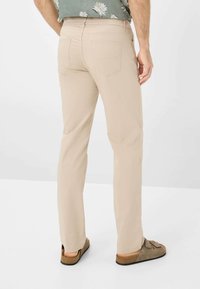 Pantaloni beige a gamba dritta realizzati in tessuto leggero. Presentano tasche posteriori e si abbinano a sandali aperti e piatti. Design semplice e pratico.
