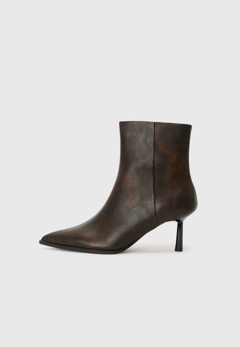 Bottine en cuir marron avec un bout pointu, un design élégant et un fine talon noir. Surface texturée avec un motif subtil.
