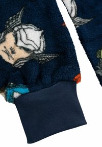 Felpa in pile con una base blu navy e stampe colorate di personaggi, dotata di polsini a coste. Tessuto morbido e testurizzato con accenti vivaci.