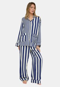 Marineblaue und weiße gestreifte Pyjama-Set aus leichtem Stoff, bestehend aus einem Hemd mit Knopfleiste und zwei Taschen vorne sowie einer locker sitzenden Hose.
