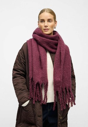 Sciarpa frangiata color borgogna realizzata in un tessuto morbido e testurizzato, indossata sopra un maglione beige e un cappotto scuro. Lunga e drappeggiata intorno al collo.