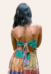 Vestido maxi de múltiples patrones con espalda baja, tirantes finos y un nudo en la parte trasera. Los colores incluyen azul verdoso, marrón, verde y dorado.