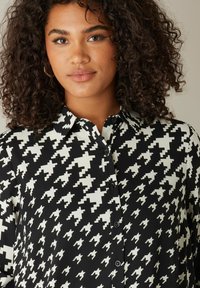 Blusa de estampado en blanco y negro con diseño de espiga, cuello, abertura de botones y tela texturizada.