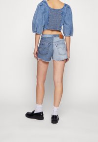 Džínové šortky v světle modré barvě s třepenými lemy, kožená nášivka vzadu, v kombinaci s modrým topem s nafouknutými rukávy a černými botami. Ponožky jsou bílé.