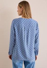 Lys blå bluse med et geometrisk mønster, lange ærmer og detalje med pleat på ryggen. Fremstillet i et blødt stof med en afslappet pasform.