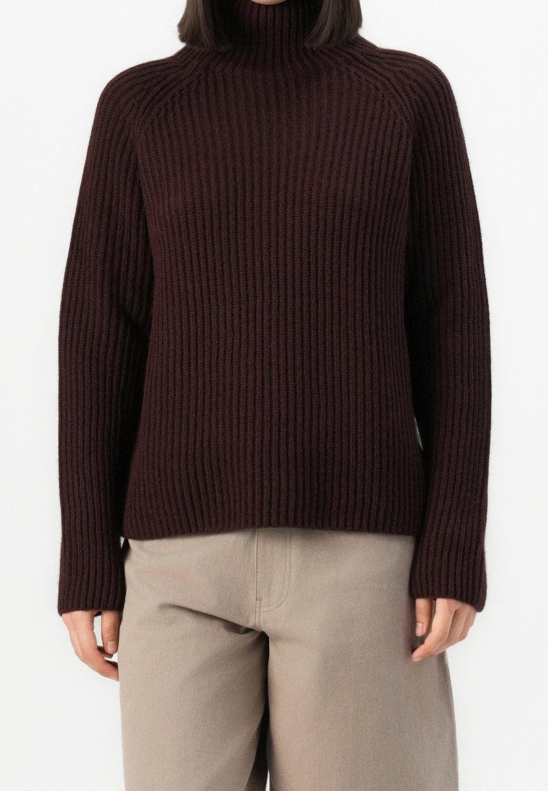 Maglione a collo alto bordeaux a costine con maniche lunghe e vestibilità morbida, abbinato a pantaloni beige chiaro a gamba dritta. Tessuto morbido e motivo distintivo.