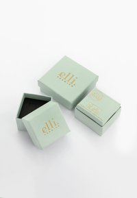 Mintgröna pappkartonger med guldtext; en låda öppen som avslöjar en svart inredning. Enkel, fyrkantig design med en mindre låda som extra.