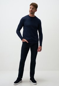Maglione a maniche lunghe blu navy con colletto rotondo abbinato a pantaloni scuri e sneakers nere. Tessuto morbido, design aderente e stile semplice.