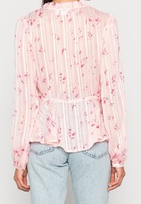 Blusa rosa chiaro con righe verticali e stampa floreale; presenta un colletto arricciato e maniche lunghe; tessuto semi-trasparente, vestibilità rilassata.