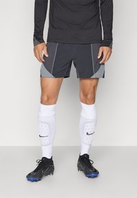 Grå atletiska shorts med kontrasterande svarta och grå paneler, i kombination med vita knähöga strumpor med en logotyp, och svarta fotbollsskor med blå accenter.