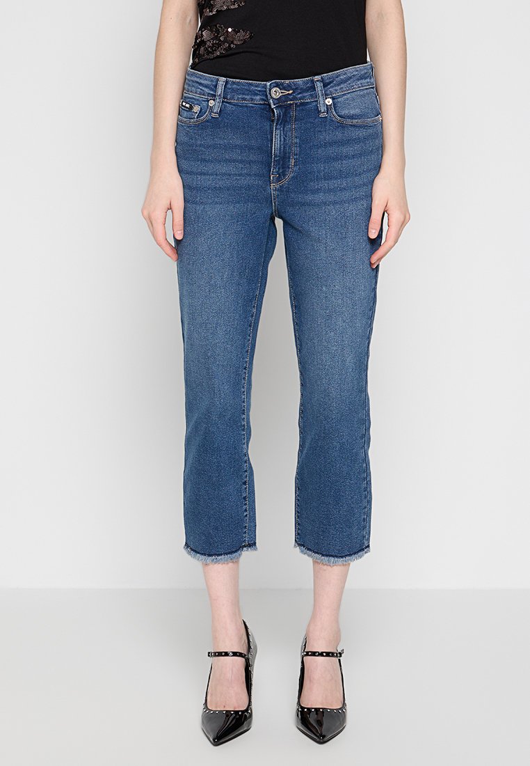 Jeans cropped in denim blu con orlo sfilacciato, design a cinque tasche e vita media, abbinati a tacchi a punta neri.