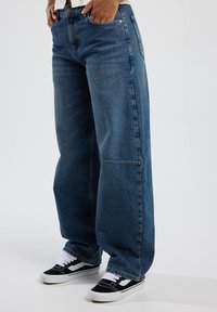 Löysät siniset farkut, joissa on korkea vyötärö, viisi taskua ja haalistunut viimeistely. Yhdistetty musta-valkoisiin matalavartisiin lenkkareihin.