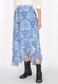 Modrá vzorovaná maxi sukně z lehkého materiálu s splývavým designem, s vysokým a nízkým lemem, stylizovaná s černými kozačkami ke kolenům.