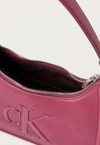 Rózsaszín bőr kézitáska ezüst cipzárral, félig nyitva, az elején nagy „cK” logóval, hozzá illő pánttal.