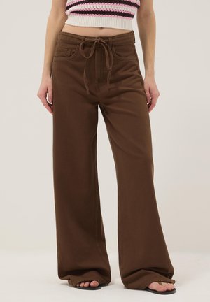 Gehäkeltes Crop-Top mit rosa, weißen und schwarzen Streifen, kombiniert mit hoch taillierter, weit geschnittener brauner Hose und schwarzen Sandalen.