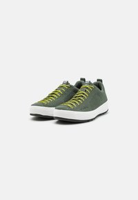 Zielone siatkowe sneakersy z żółtymi sznurowadłami, białą podeszwą środkową i czarną gumową podeszwą; mają dwa uchwyty na pięcie ułatwiające zakładanie.