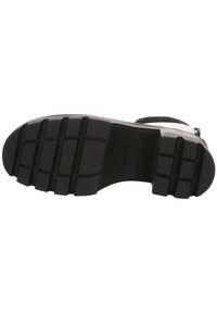 Suela de zapato de goma negra con un patrón texturizado, que presenta surcos y estrías profundos para una mejor tracción. Marcada con "Calvin Klein Jeans."