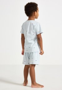 Pigiama corto in cotone azzurro chiaro a maniche corte con piccoli motivi a barche. La parte superiore ha un collo tondo; i pantaloni corti hanno un'elastico in vita.