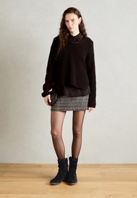 Suéter negro de canalé superpuesto sobre una camisa negra con cuello, combinado con una falda corta de estampado y botas de ante oscuro con caña ancha. Bolsa de hombro sencilla.