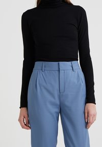 Col roulé noir à manches longues associé à un pantalon taille haute bleu clair, en tissu lisse et coupe ajustée.