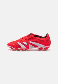 Red soccer cleat with a textured upper, white stripes, and black accents; features a strap across the laces for improved fit and stability.
