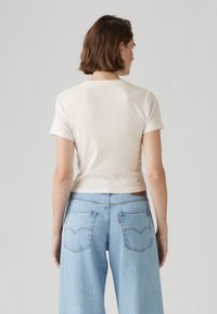 En blandning av bomull, kortärmad, kort beige t-shirt som kombineras med ljusblå vida jeans med bakfickor och subtila sömdetaljer.