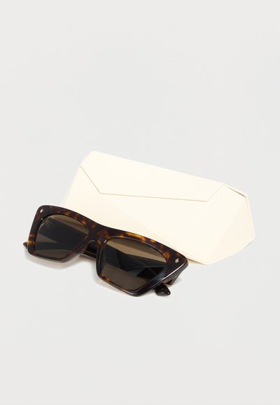 Σκούρα ορθογώνια γυαλιά ηλίου με μοτίβο χελώνας και σκοτεινούς φακούς τοποθετημένα μπροστά από μια μπεζ, μαλακή προστατευτική θήκη.