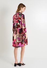 Vestido multicolorido en una mezcla de rosa, marrón y crema con patrones geométricos y florales audaces. Manga larga y detalle de cintura ajustada.