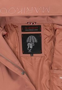 Light pink outerwear with a smooth texture, featuring a logo in capital letters and a black inner label with a cartoon design and size tag.